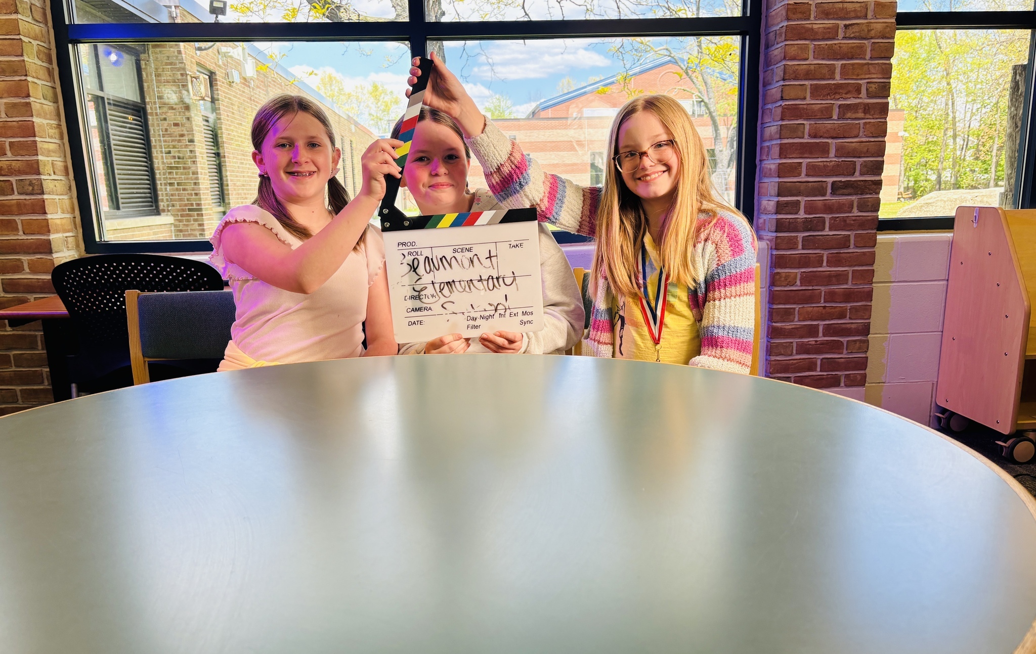 three students smiling at camera with countdown clapper